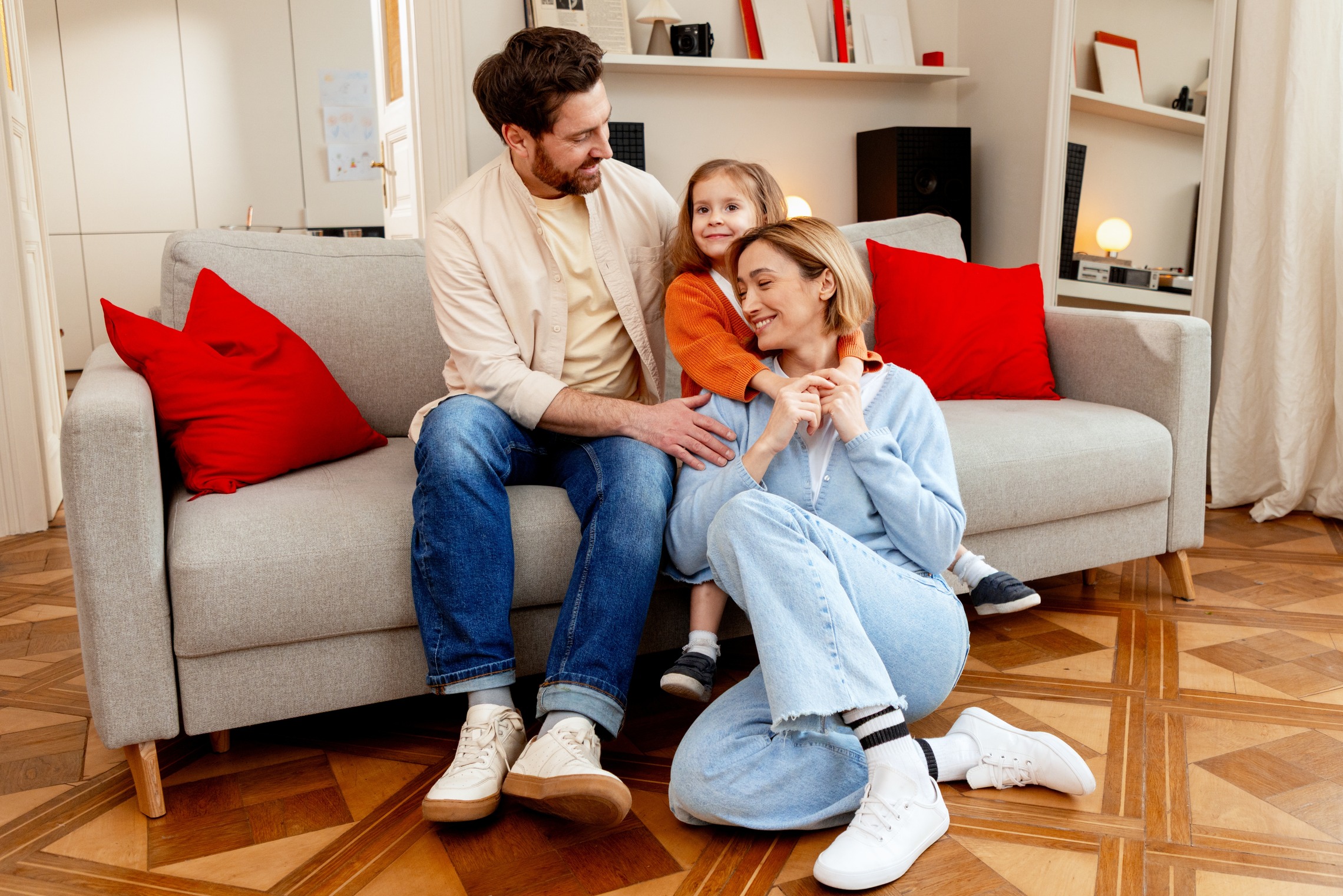 bardziej formalne Das Bild zeigt einen Mann und ein Kind, das auf dem Sofa sitzt und eine Mutter, die darunter kniet.